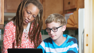 Foster parent helping child in eyeglasses working on laptop